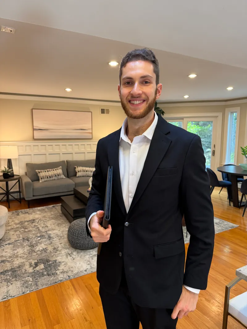 Jared Cohen, REALTOR®, smiling and holding a leather folder in a bright living room