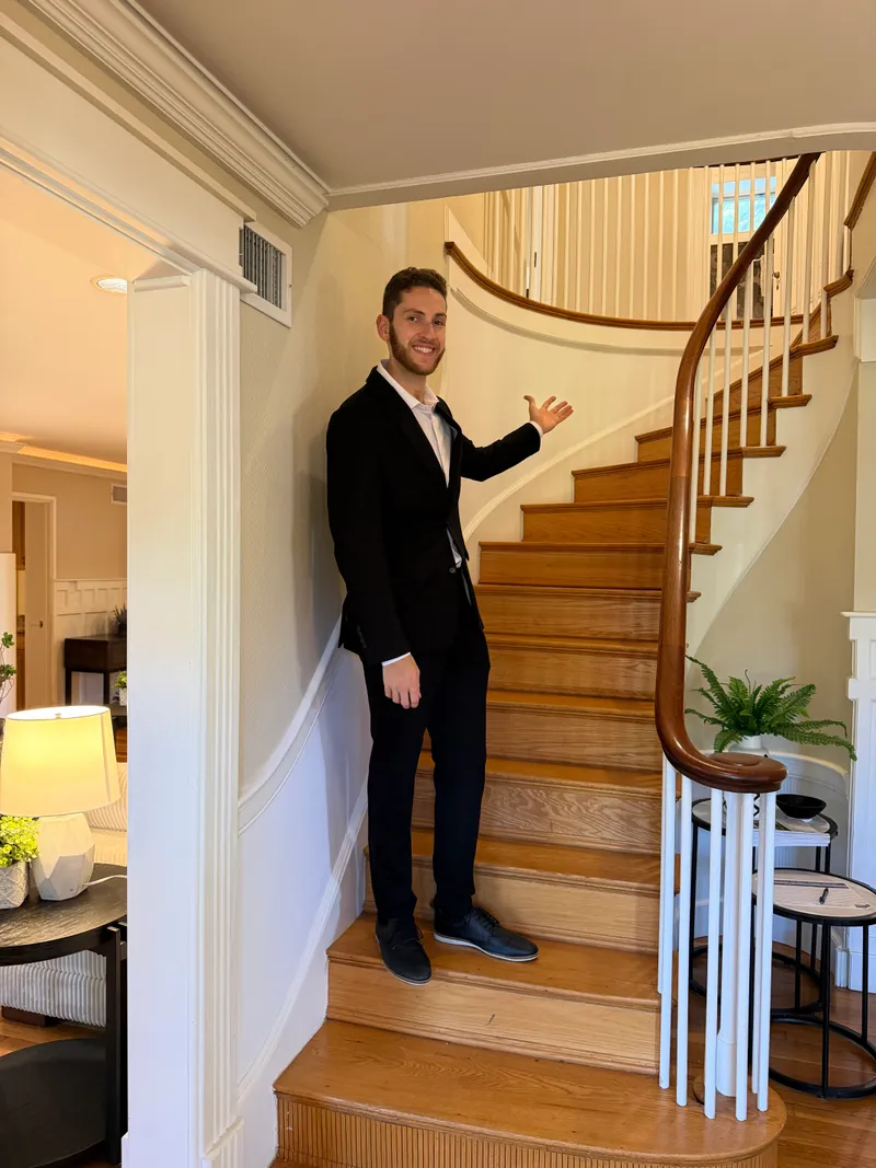 Jared in a front hall, gesturing toward a curved staircase